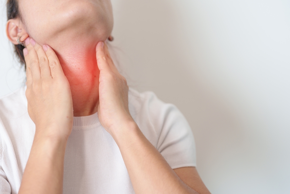 Person holding neck with red highlight indicating thyroid pain or swelling